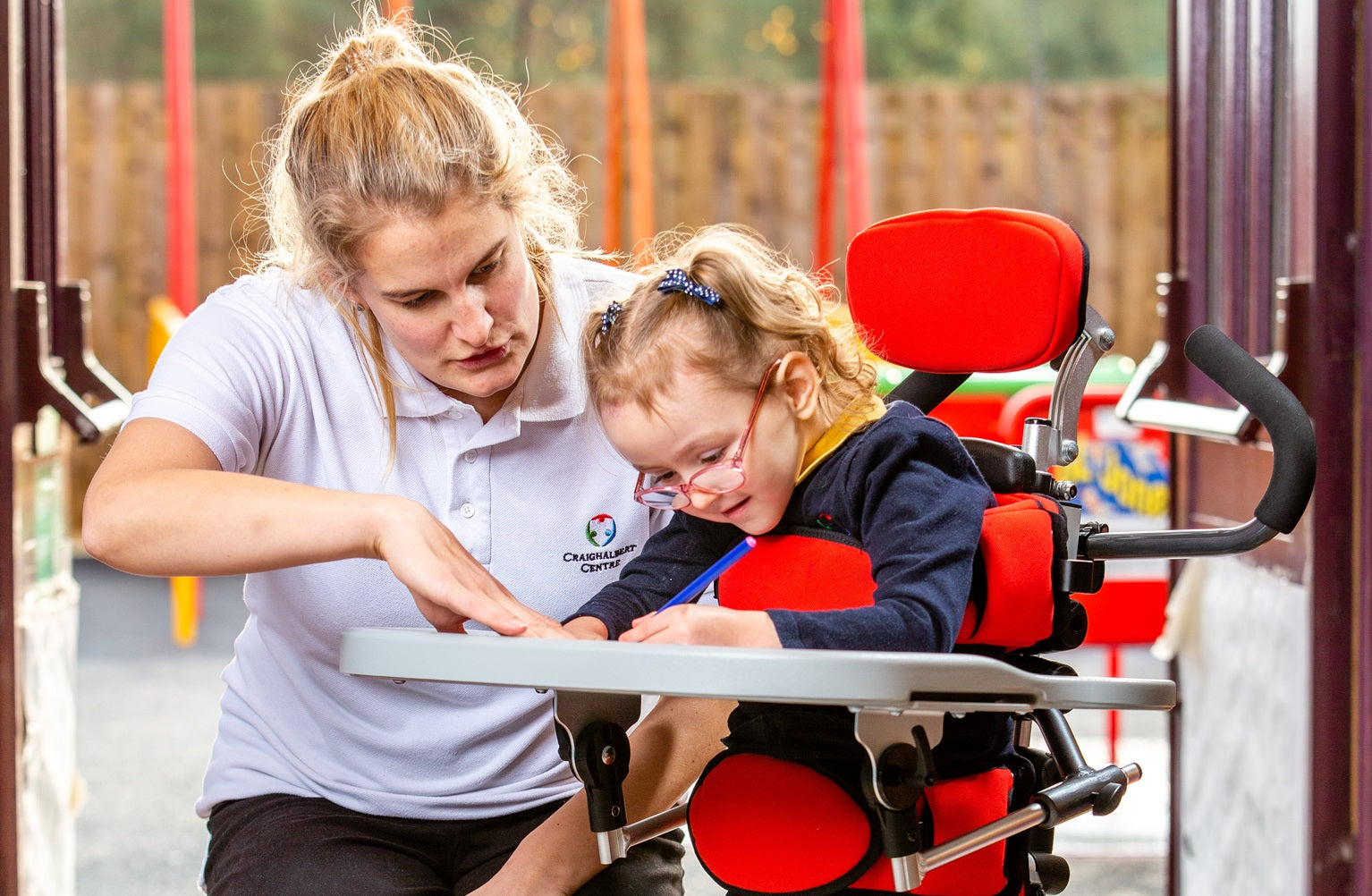 Clinician looks at something with child in Leckey Squiggles+ Stander.