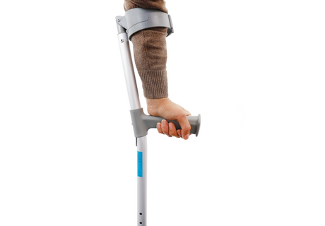 A person’s arm in a brown sweater is shown using a gray forearm crutch against a white background.