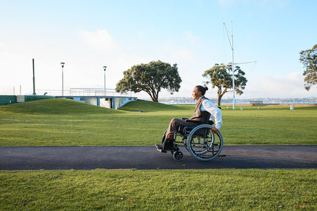 Man in wheelchair on path through a lush green park.